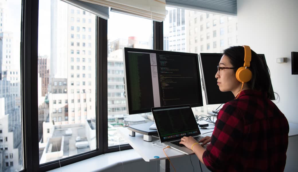 Engineer at a standing desk working across code on two monitors